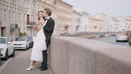 Side view of caring lovely just married couple embracing by the granite sidewalk. Action. Elegant bride and groom outdoors in the street.の写真素材