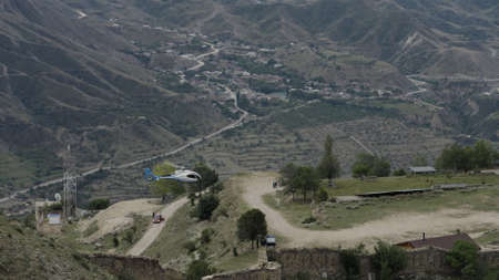 Aerial view of a helicopter flying above the small village located in mountains. Action. Hilly...