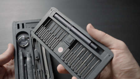 Set of screwdrivers with gray handles in a box in male hands on a dark table background. Action....