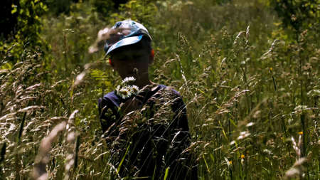 Portrait of a little bot standing with his eyes closed in long grass. Creative. A boy in a summer meadow with the grass swaying in the wind.の写真素材