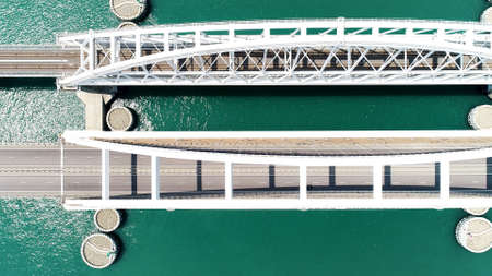 Top view of big bridge over green river. Action. Big white bridge with highway and traveling cars. Beautiful turquoise river with highway on bridgeの写真素材