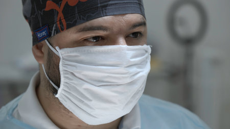 The face of a male surgeon in a sterile mask in operating room. Action. Close up of a doctor during surgery.の写真素材