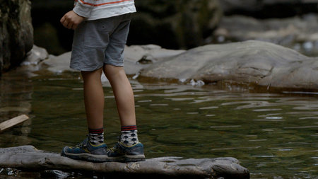 Legs of a teenager young boy in sportswear on a rock above river. Creative. Boy on a stone above...