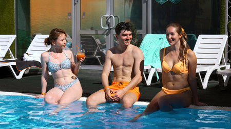 Beautiful young people having fun in swimming pool. Clip. Friends communicating and sitting on the...