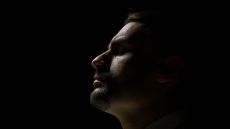 Young serious handsome businessman combing his hair. Stock footage. Side view of a concentrated man in a dark room.の写真素材