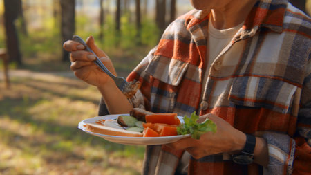 Woman standing with barbecue plate in nature. Stock footage. Close-up of woman eating standing with plate in forest. Relaxing with barbecue and vegetables at barbecue on sunny summer dayの写真素材