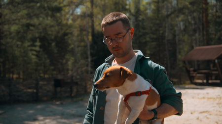 Man holds dog in hands in woods. Stock footage. Man holds Jack Russell terrier in arms. Man holds dog in arms in park on sunny summer dayの写真素材