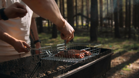 Close-up of men frying chicken on grill in forest. Stock footage. Delicious grilled chicken with barbecue on sunny summer day. Men cook chicken on grill and relax in forestの写真素材