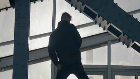 Guy dancing hip hop on bridge. Action. Cool dance in modern style of street dancer. Young man dances in modern style at steel beams of buildingの写真素材