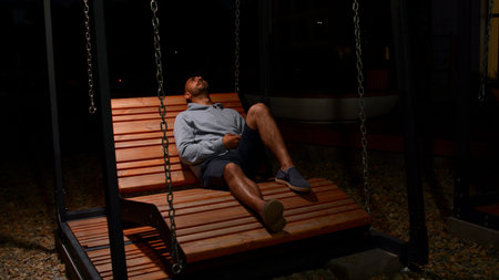 A man resting in the night. Media. An adult cute brunette in shorts who sits on a bench at night.の写真素材