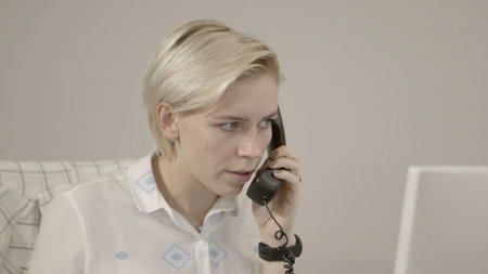 A woman at work. Stock footage. A cute secret in a shirt is talking on the phone and looking at the client base in the computer.の写真素材