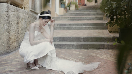 Cute walking couple sitting on the stairs. Action. Happy newlyweds filming on the street in wedding costumes.の写真素材