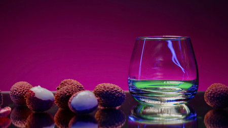 Green cocktail with syrup. Stock clip. Pink background with backlight next to the lying lychee and pouring a bright drink.の写真素材