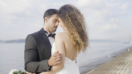 Beautiful bride and groom standing on the summer embankment. Action. Romantic young family couple on their wedding photosession.の写真素材