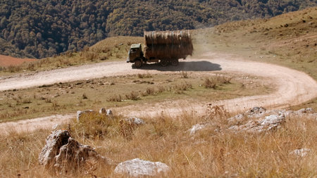 Vehicle loaded by haystacks passing at rural area. Creative. Sunny day and a valley with growing grass.の写真素材