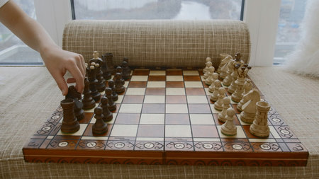 Childs hand makes chess move. Creative. Expensive chess board with pieces by window. Place on windowsill for relaxing with chess and childの写真素材