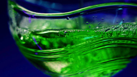 Bartender pours portion of alcohol in the cocktail glass. Stock clip. Making green cocktail at the nightclub isolated on a dark blue wall background.の写真素材