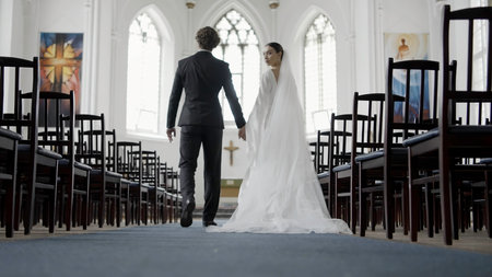 Bride and groom at the wedding ceremony in modern church. Action. Woman and man walking together towards the altar among the empty rows of seats.の写真素材