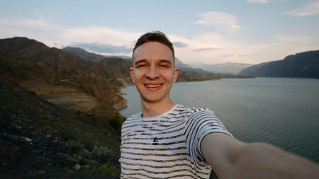 Young hiker traveler man taking selfie at mountain top. Action. Young happy man with mountains and...