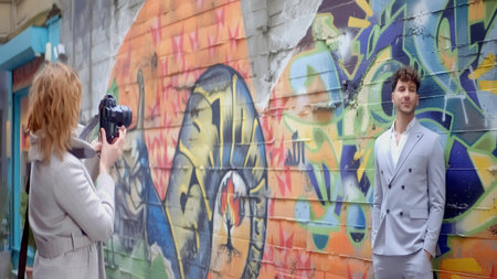 Photographer making photo of a young man in suit on a graffiti wall background. Action. Photo shooting and street art.の写真素材
