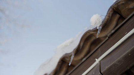 Icicles hang from a roof and melt with drops of water falling down. Action. Concept of coming spring.の写真素材