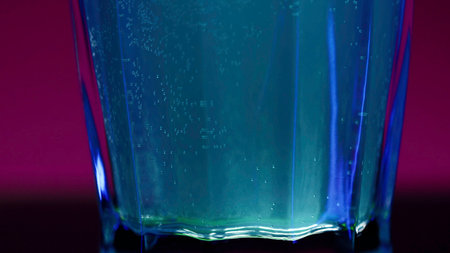 Close up of blue alcoholic cocktail standing on a bar counter on a pink wall background. Stock clip. Concept of alcoholic addiction.の写真素材