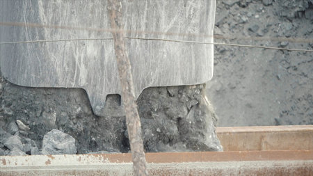 Close-up of excavator bucket loading ore in the dump-body truck. Mining industry.