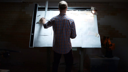 Rear view of male architect working on blueprint. Rear view of engineer drawing project of business...