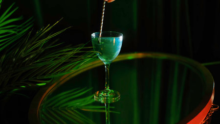 Close up of Aviva green wine with pearl standing on a glass surface table near the plant under green light. Stock footage. Composition in green colors and a hand stiring shining wine with a spoon.の写真素材