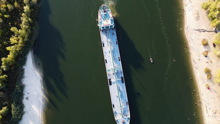 Top down view of a cargo ship in a canal of green color. Long white inland vessel floating down the...