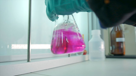Close-up of flask with chemical liquid. Clip. Laboratory assistant conducts experiments with chemical liquid that changes colors. Chemical process in transparent flask in laboratory.の写真素材