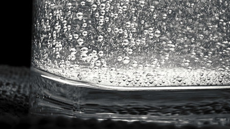 Close-up of glass filled with sparkling water standing on the knitted small mat on the dark background. Stock footage. Monochromeの写真素材