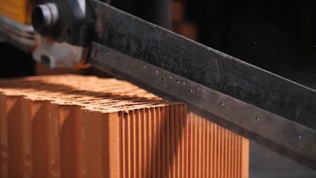 Professional saw for cutting bricks. Close-up of unknown worker using a professional saw cutting the brick at construction site.の写真素材