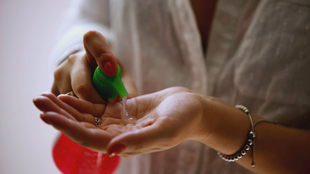 A woman squeezes liquid from a vial onto her hand. ART. Colored jar and woman's hands close-up.Woman uses disinfectant during a pandemic.の写真素材