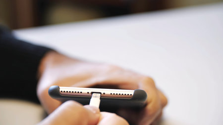 Close up of hand inserting a USB cable charger into a mobile phone. Close up mans hand inserting a...