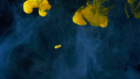 Beautiful yellow paint drops spreading in water. Close up of clouds of yellow and blue ink isolated on black background, art concept.の写真素材