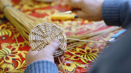 Hands weaving the bottom of a straw basket. ART. A man weaves a round part of straw and twigs with his hands. Crafts are learned at the Russian festival.の写真素材
