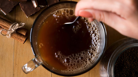 Close up of preparing hot beverage. Hand holding coffee spoon and stirring hot coffee on vintage old...