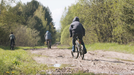 Rear view of children riding bicycle on rural road. Summer lifestyle moment of a happy childhood, children having fun and riding bicycles along the summer green forest.の写真素材