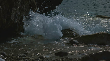 Close-up of small waves crashing on rocks. Creative. Stone beach with splashing waves on cloudy day....