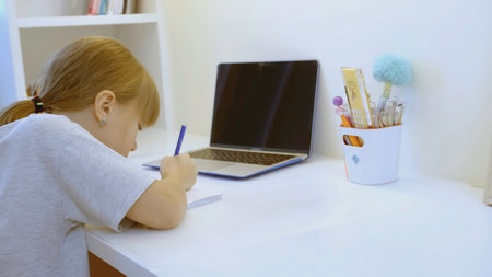 Girl is sitting at workplace in children's room. Creative. Girl at table is going to study. Girl is engaged at desk in room. Children's room.の写真素材