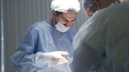 Close up of male surgeons at work. Action. Side view of concentrated doctors looking down to the...