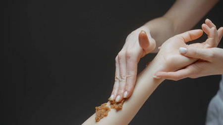 Woman enjoying a sugar sea salt natural body scrub exfoliation treatment with professional beautician. Action. Concept of beauty and body care.の写真素材