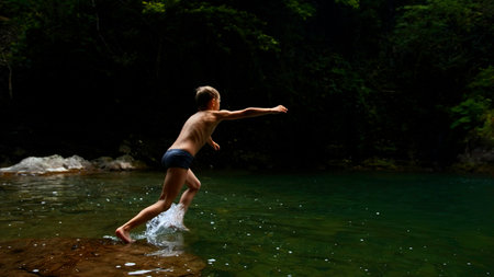 Boy child jumping in cold mountain river on a summer day. Creative. Hiking in summer jungles.の写真素材