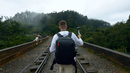 Caucasian traveler man recording video of green mountain landscape. Action. Man walking on railroad...