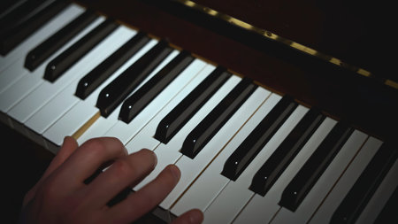Close-up of hand playing piano. Media. Light falling on hand playing piano. Lonely hand is playing...