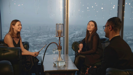 Man meets women in hookah bar. Media. Man sits down with young women to meet in restaurant. Company of elegant adults in hookah restaurantの写真素材