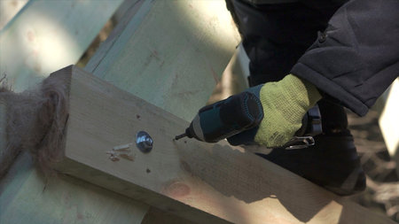 Close-up of builder drilling wooden structure. Clip. Man drills wooden beams of house under construction. Construction of wooden country houseの写真素材