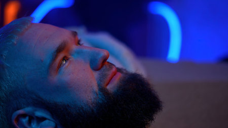 Close up side view of a bearded man looking up and thinking of something. Media. Young man with neon...