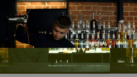 The barman preparing perfect cocktail, standing behind the bar counter. Media. Many bottles of alcohol on the background.の写真素材